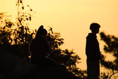 Silhouette man and woman standing against sky during sunset