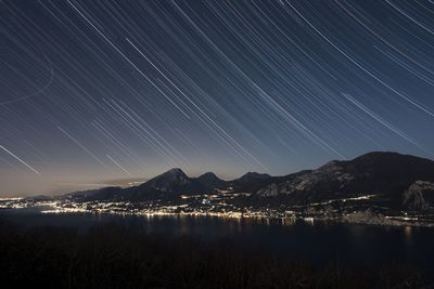 Light trails above lake and mountains at night
