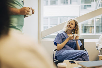 Smiling healthcare worker with coffee cup sitting on chair during break in hospital