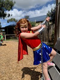 Portrait of girl dressed as superwoman with red cape on climbing frame at a playground