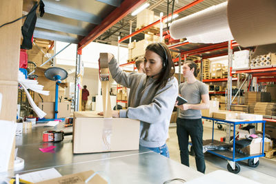 Woman packing box while coworkers discussing in distribution warehouse