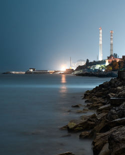 Sea by illuminated buildings against clear sky