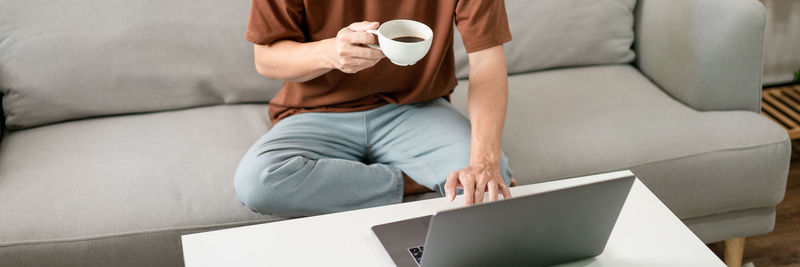 Midsection of woman using digital tablet while sitting on sofa at home