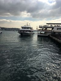 Boats sailing in calm sea against cloudy sky