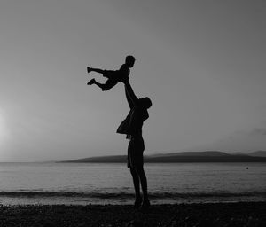 Silhouette father lifting son at beach against sky