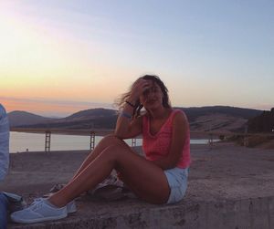 Young woman sitting on retaining wall during sunset