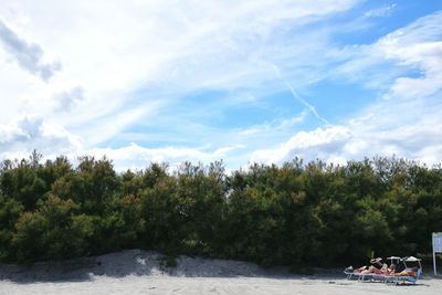 View of trees by calm lake against cloudy sky