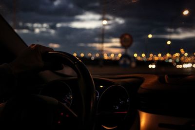 Close-up of hand on illuminated car against sky in city