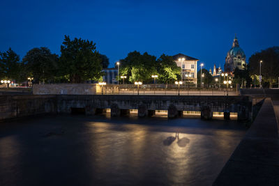 Illuminated building by river against sky at night