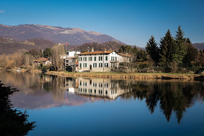 Reflection of building and trees by lake against sky