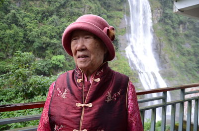 Woman looking away while standing against waterfall