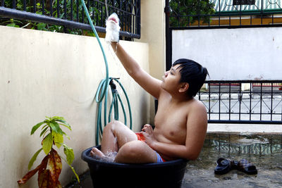 Asian boy cooling down in a water basin and a hose as a makeshift shower to beat the summer heat.