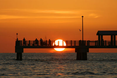 Silhouette people on pier over sea against sky during sunset