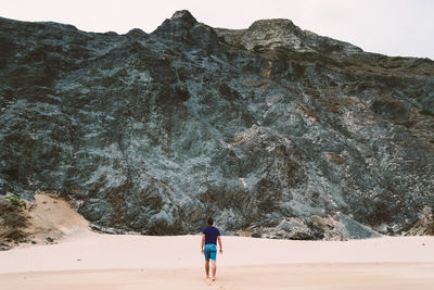 Rear view of man walking at beach against mountains