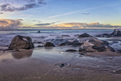 Rocks on beach against sky during sunset