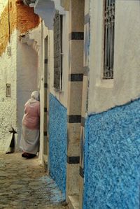 Rear view of woman standing in alley amidst buildings