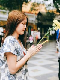 Profile view of young woman holding flower and candle while praying at temple