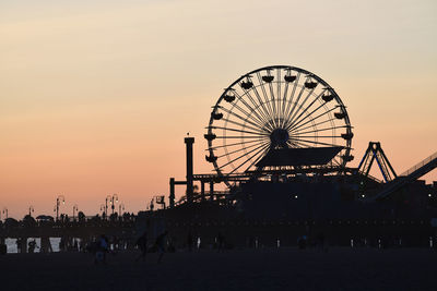 Ferris wheel at beach against sky during sunset