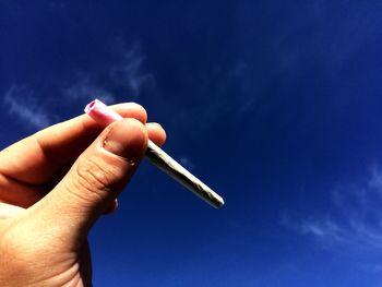 Cropped image of hand holding marijuana joint against sky