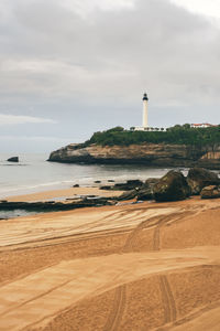 Lighthouse on beach by sea against sky