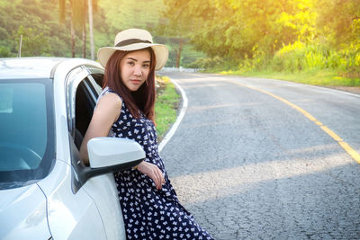 Portrait of young woman standing by car on road