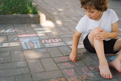 Little preschool boy draws with colorful chalks on the ground.