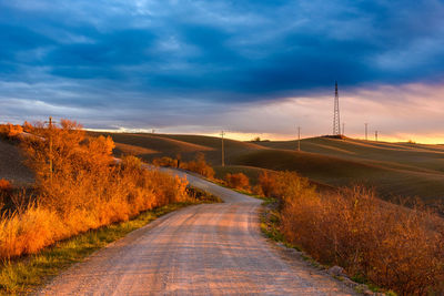 Road amidst field against sky during sunset