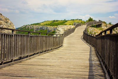 Boardwalk leading towards footbridge against sky