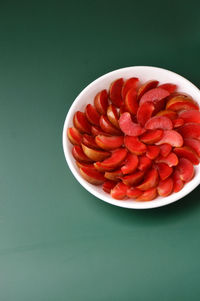 Composition of slices of vietnamese red plums on a white plate against green background