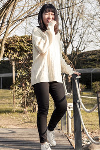 Full length portrait of smiling young woman standing at park