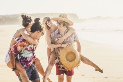 Boyfriends piggybacking girlfriends at beach against clear sky