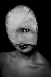 Close-up portrait of topless young woman face wrapped in bandage against black background