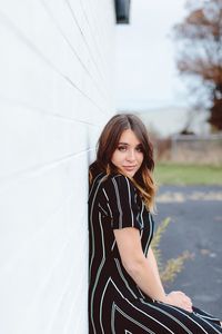 Side view portrait of young woman standing by white wall