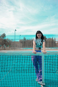 Portrait of woman standing at tennis court against sky