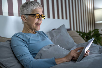 Mature woman wearing blue light blocking glasses, looking at tablet screen