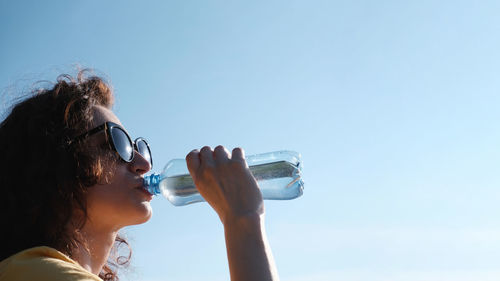 Girl with glasses drinks water from a bottle in hot weather.