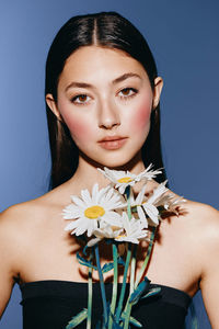 Portrait of young woman with flowers against blue background