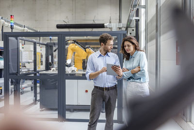 Colleagues in high tech company controlling industrial robots, using digital tablet