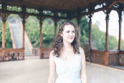 Beautiful curly hair young woman in light blue simple dress in pavilion in a garden. summer portrait