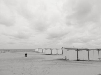 Beach huts on sand against cloudy sky