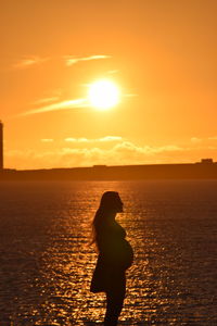 Silhouette pregnant woman standing at beach during sunset