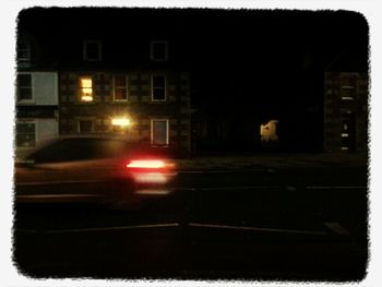 Illuminated road by house against sky at night