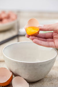 Cropped image of hand pouring egg in bowl