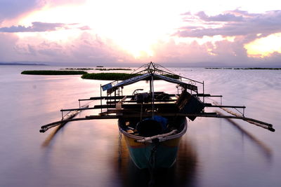 Outrigger boat on sea against cloudy sky during sunset