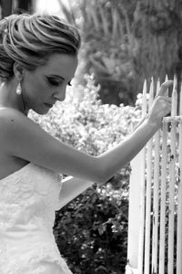 Side view of thoughtful bride looking down while holding fence at park