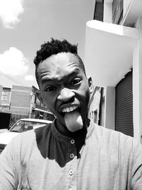 Portrait of young man sticking out tongue against buildings