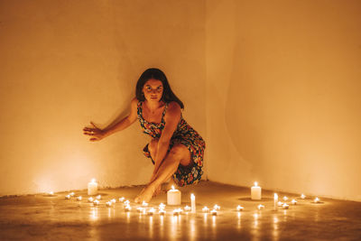 Young woman sitting against illuminated wall