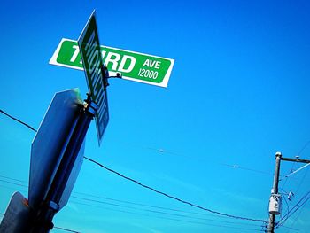 Low angle view of road sign against clear blue sky