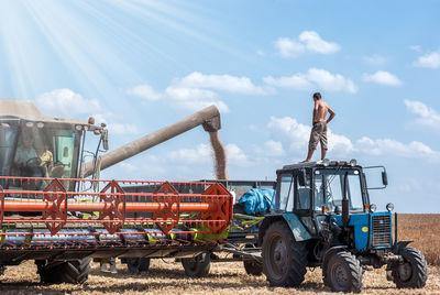 Farmer standing on combine harvester against sky