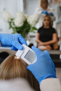 Close up view of female trihologist examines head skin of woman with special dermatology equipment